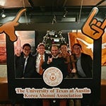 Longhorn alumni posing behind UT branded frame.